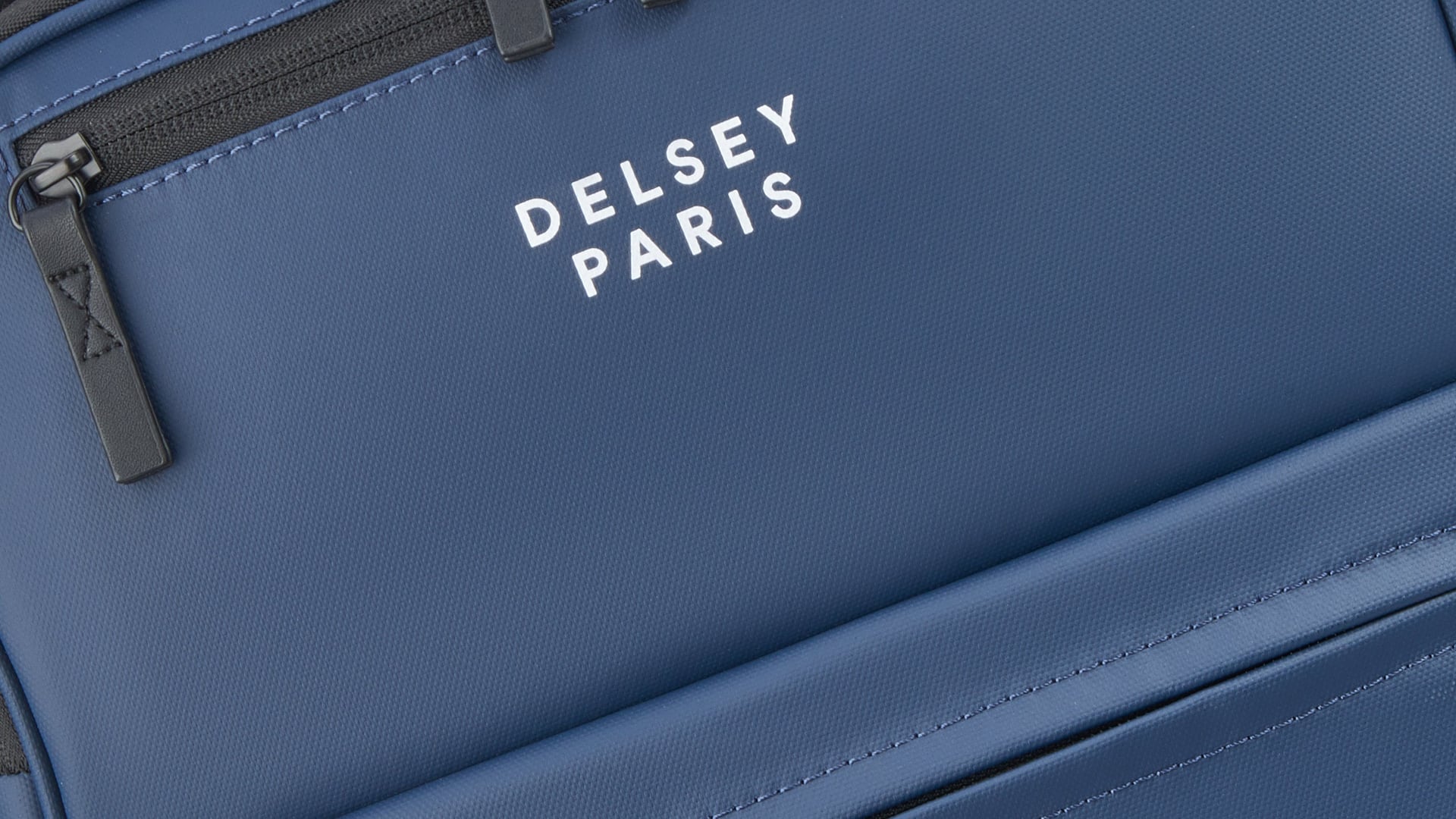 Gros plan sur la poche avant zippée d’un sac à dos Maubert 2.0 bleu, logo DELSEY PARIS imprimé en blanc