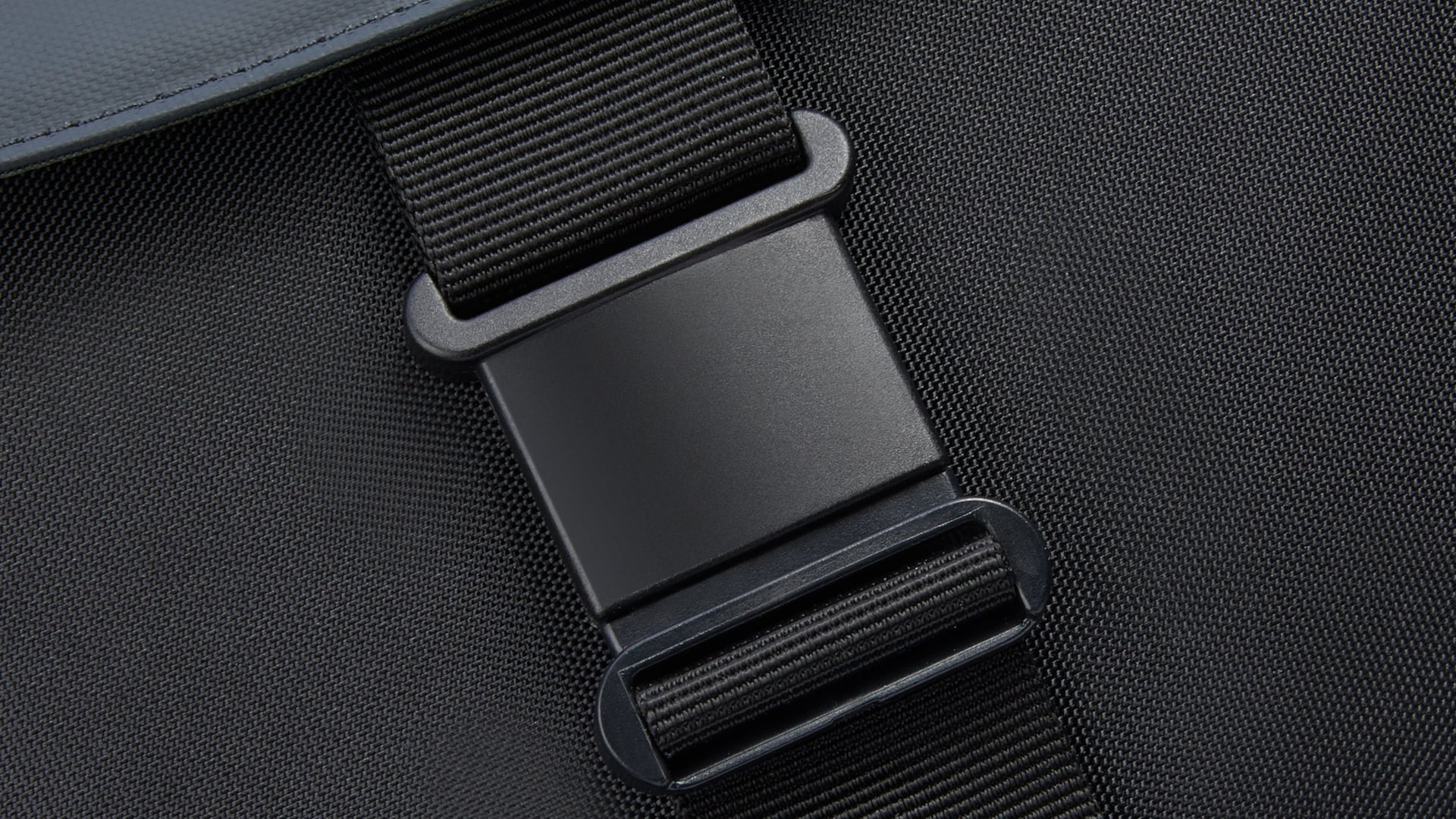 Gros plan sur la boucle sécurisée du sac à dos Securflap noir, sous son rabat gris ardoise